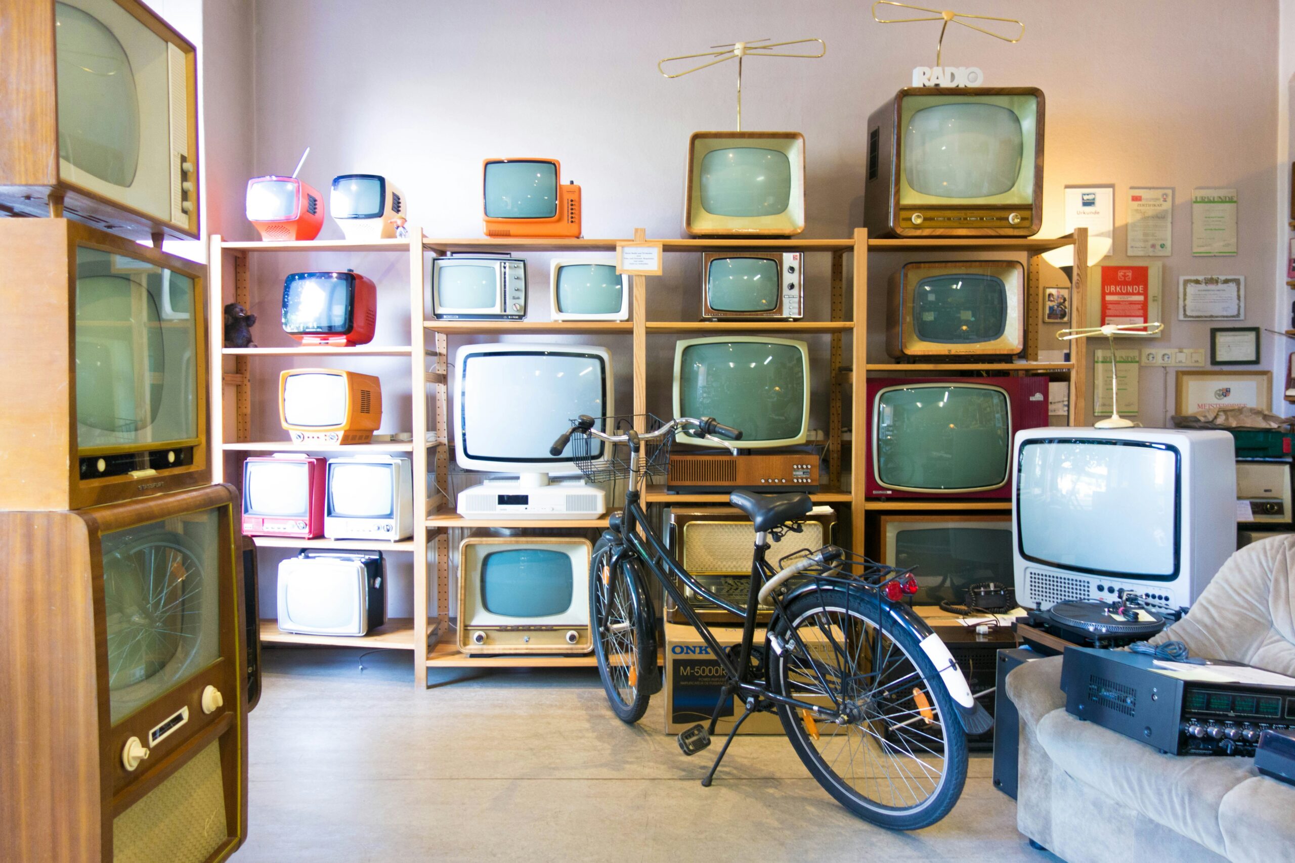 a light room with vintage television sets of different sizes stacked against a wall with a bike in front